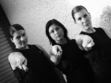 3 girls holding drumming sticks pointing towads camera